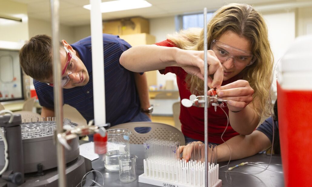 Two Denison University students in safety goggles working with lab equipment in a science lab