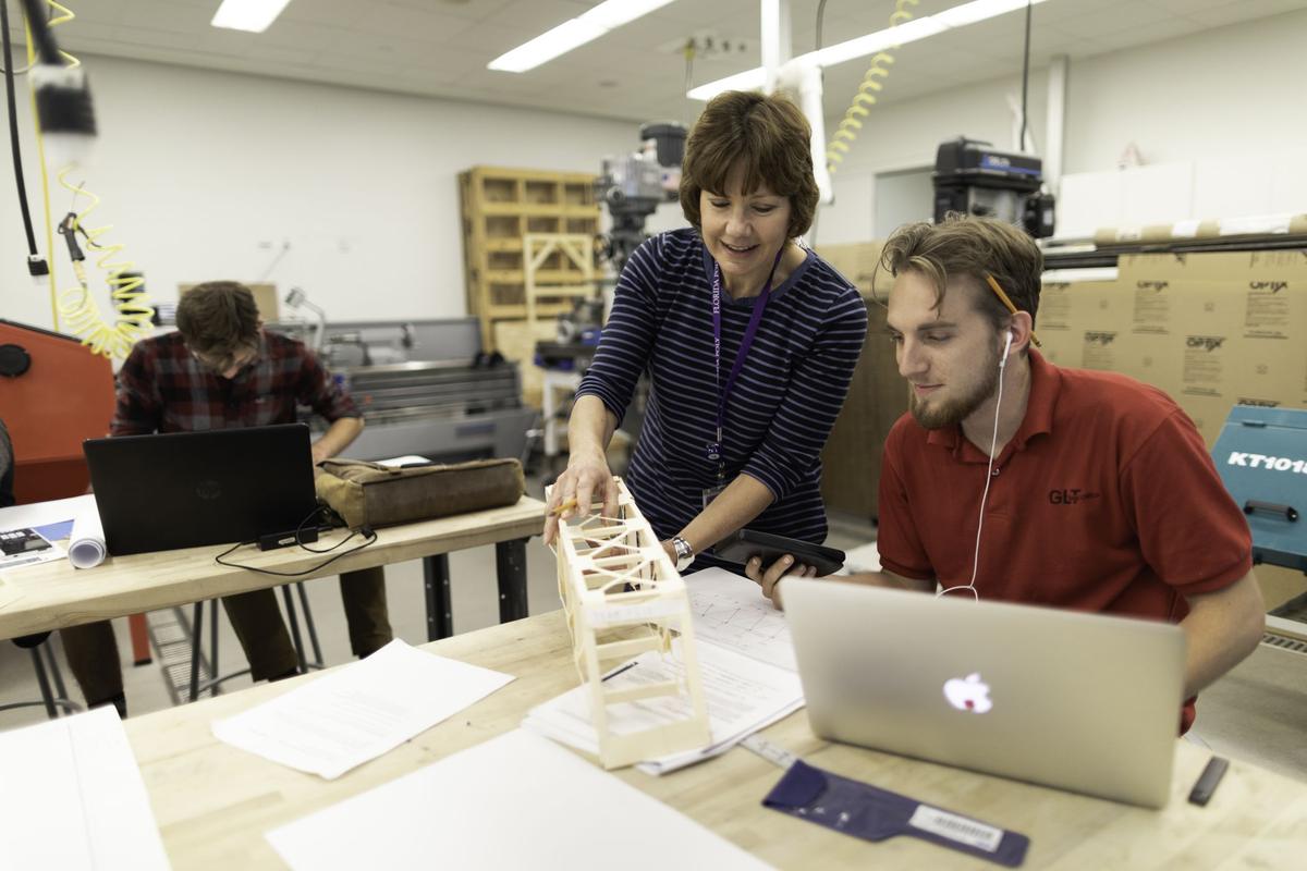 A Florida Poly faculty member reviews a student's truss model in an engineering lab